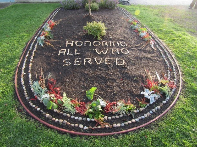 A tribute to veterans which reads “Honoring All Who Served” made of rocks in a garden.