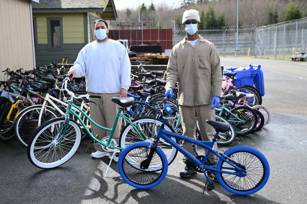 Two incarcerated individuals stand next to bikes they repaired