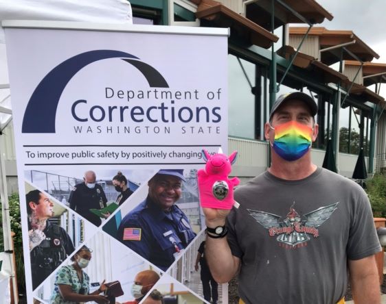 Person with rainbow mask stands next to Corrections recruitment poster.