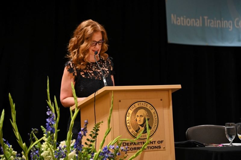 Woman stands at podium, addressing the audience.