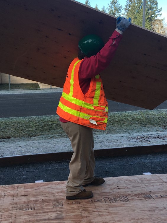 Incarcerated Individual carrying large rectangle of plywood overhead.