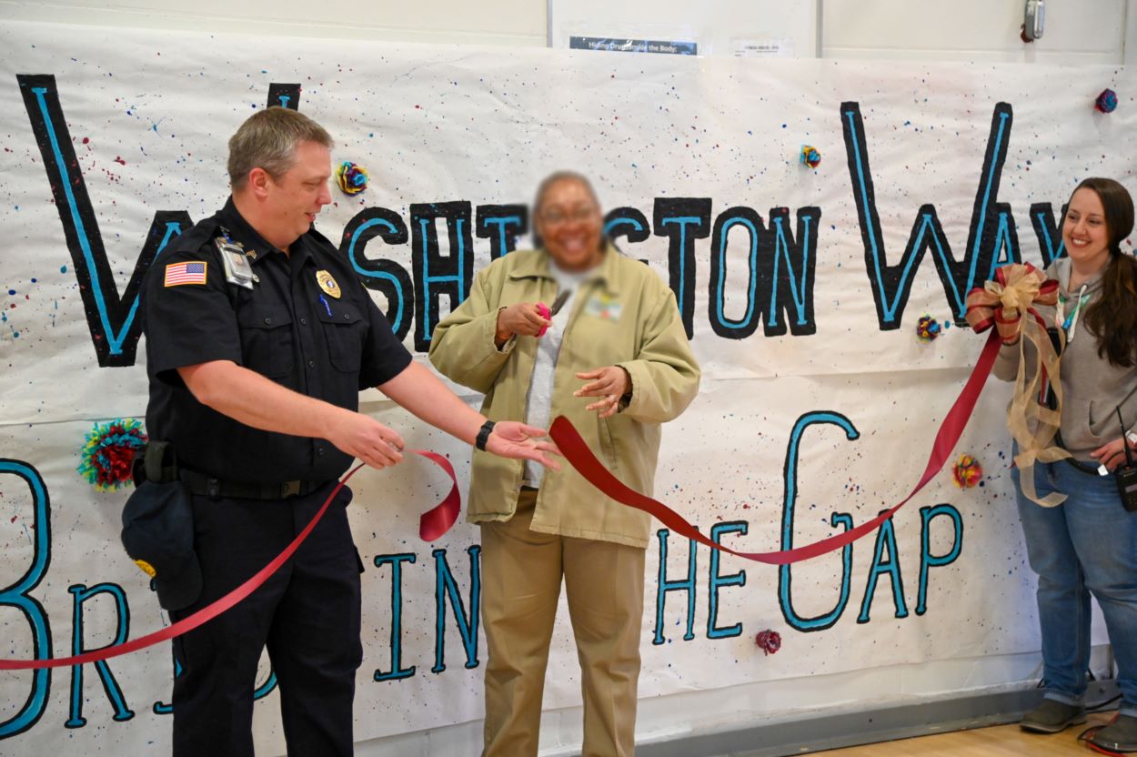 A woman cutting a long ribbon held by two other people.