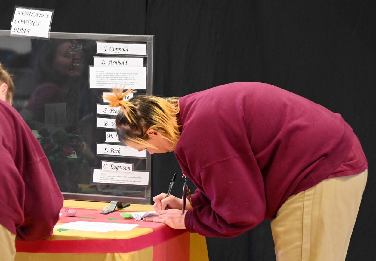 A woman bent over, writing on a table.